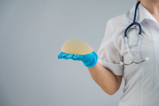 Female doctor aesthetic surgeon holding a breast implant on a white background