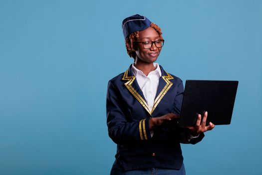 Optimistic african american flight attendant wears uniform doing online shopping and bill paying with laptop. Female stewardess using notebook during break time at work.
