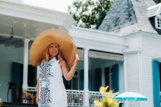 the woman in the big hat is smiling. a beautiful girl in a big hat and white dress smiles outside an old colonial building on the island of Mauritius.