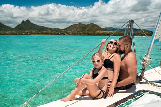 a happy family in swimsuits sits on a catamaran in the Indian Ocean. portrait of a family on a yacht in the coral reef of Mauritius.