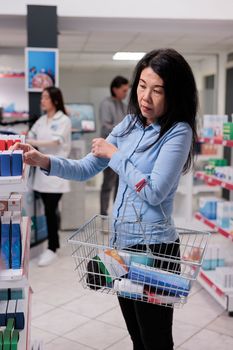 Elderly customer putting box of pills in basket to buy prescription medicine and medical products. Client taking pharmaceutical drugs package to cure disease, healthcare supplies capsules.