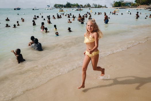 a little girl runs along a tropical beach with locals on the island of Mauritius.a girl on the beach of the Indian ocean and unrecognizable locals of the island of Mauritius.