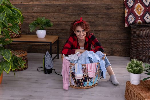 Happy and smiling girl that she will be able to quickly iron clean clothes after washing. Full of vigor and strength to work. A wall in the house made of boards.