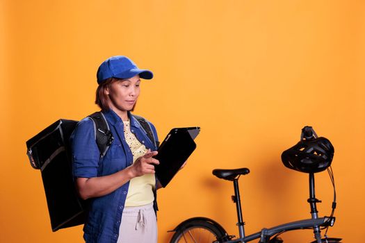 Slide view of cheerful deliverywoman holding tablet computer checking client location to deliver takeaway pizza. Restaurant courier carrying takeout food backpack. Food service and transportation