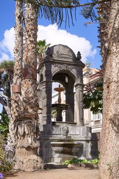Outdoor fountain with medieval architecture and palm trees at Plaza del Espiritu Santo in Vegueta, Las Palmas de Gran Canaria, Spain