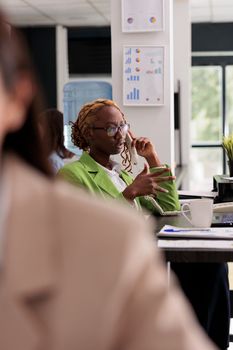 Employee discussing company financial strategy with business partners on landline phone, working in start up job coworking space. Office manager answering call, having remote conversation