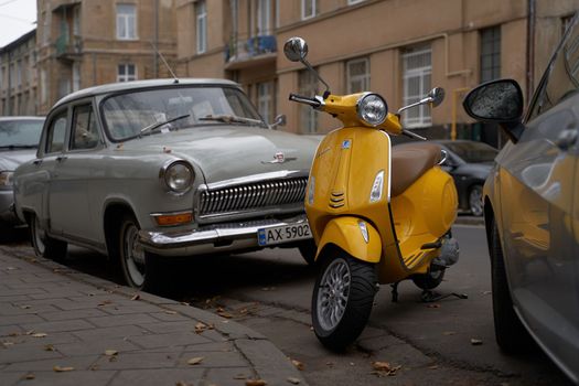 Lviv, Ukraine - November 2, 2022: Yellow Vespa Elettrica electric scooter released circa 2019 by Piaggio company in Italy parked on the street between cars.