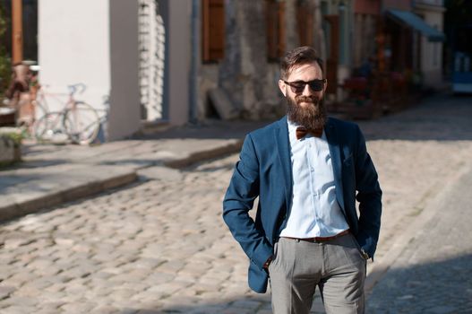 Stylish man with beard wearing a jacket, shirt and bow tie on a sunny day