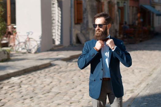 Stylish man with beard wearing a jacket, shirt and bow tie on a sunny day