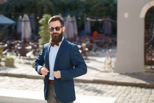 Stylish man with beard wearing a jacket, shirt and bow tie on a sunny day