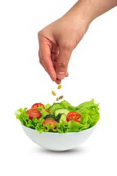 White bowl of salad with fresh cucumbers, tomatoes, iceberg salad leaves and male hand pouring oil with spoon over salad isolated on white background