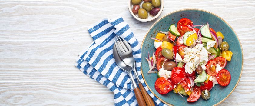 Greek fresh healthy colorful salad with feta cheese, vegetables, olives in blue bowl on rustic white wooden background top view, Mediterranean diet, traditional cuisine of Greece. Space for text