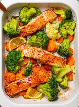 Top view close up of healthy baked fish salmon steaks, broccoli, cauliflower, carrot in casserole dish. Cooking a delicious low carb dinner, healthy nutrition concept.