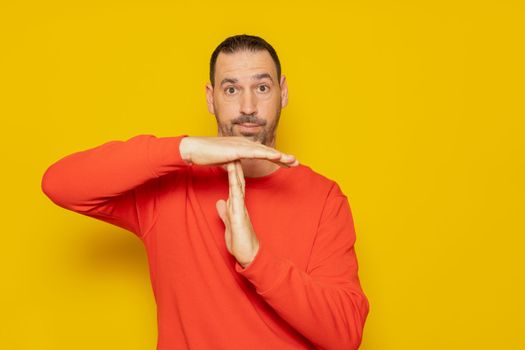 Latino man with a beard in a red sweatshirt making the time-out gesture, he needs a break from the pace of life demanded of middle-class people. Isolated on orange background