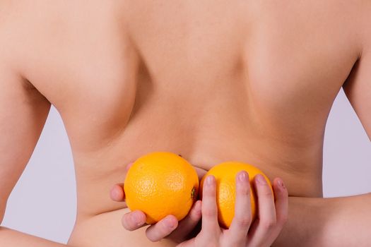 Slim woman is holding orange. Perfect female back without any cellulite.