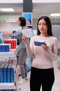 Young customer analyzing packages of pills in pharmacy, looking at medicaments in boxes to buy prescription treatment. Client examining medical drugs and healthcare supplies to cure disease.