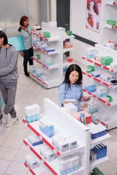 Elderly person reading pills box leaflet before buying healthcare products from drugstore shelves. Pharmacy client looking at medicaments and vitamins packages, cardiology drugs.