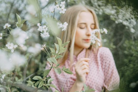 Blonde girl on a spring walk in the garden with cherry blossoms. Female portrait, close-up. A girl in a pink polka dot dress