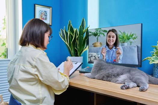 Middle aged woman having video conference call chat with young female on computer screen, in home office. Teacher, business coach, psychologist, therapist looking at webcam, virtual online meeting