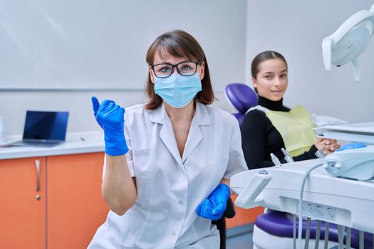 Portrait of female dentist looking at camera with young teenage girl patient sitting in dental chair. Dentistry, hygiene, treatment, dental health care concept