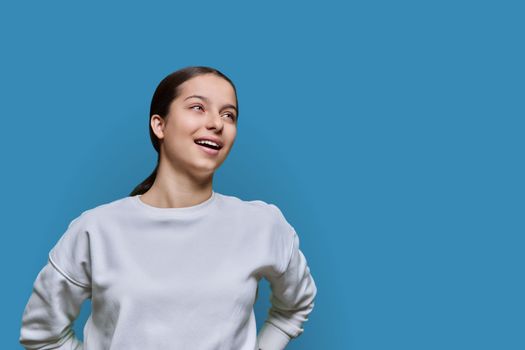 Portrait of teenage smiling female looking up on blue color background, copy space. Adolescence, education, high school, youth 15, 16 years old concept