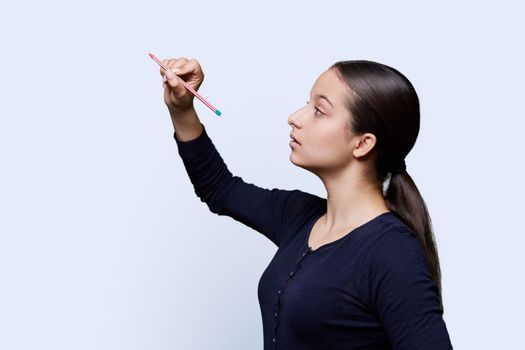 Teenage girl student with a pencil draws on an abstract screen, copy space, white studio background.