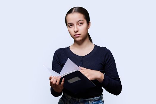 Teenager female student with notebook looking at camera on white studio background. Education, high school, college, knowledge, adolescence concept