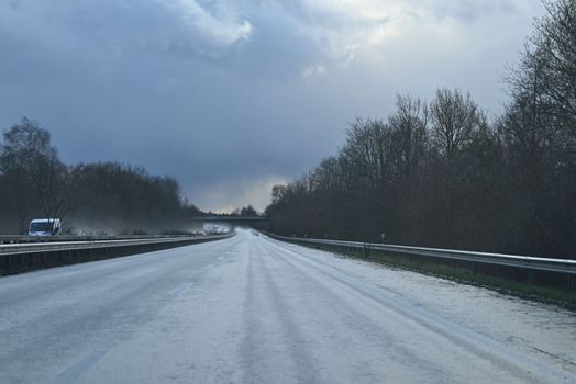 Wet highway with trees at the side against a dramatic sky