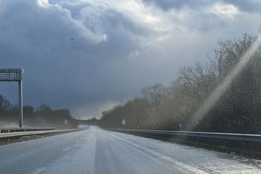 Wet highway with trees at the side against a dramatic sky