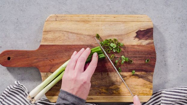 Cutting organic green onions on a wood cutting board.