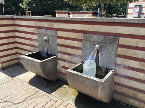 Locals in town to gather water from a public drinking fountain with fresh water. High quality photo