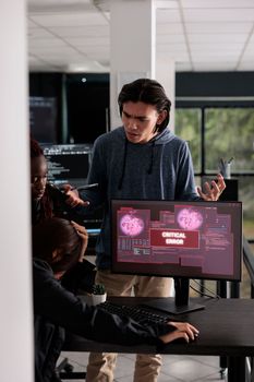 Multi ethnic team of it programmers having hacked server and security breach alert on pc display, trying to solve hacking problem. Encountering critical error message flashing on screen.