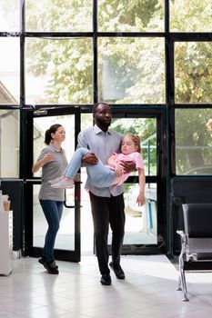 Worried father walking in hospital waiting room holding fainted unconscious daughter in arms trying to get help. Caucasian little child faints and collapses. Health care service and concept