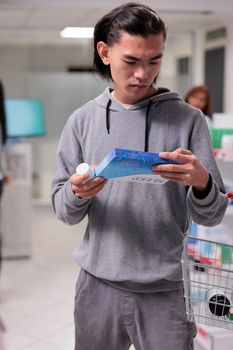 Male customer looking at box of sleeping pills in drugstore, buying pharmaceutical sedatives to help with health care. Reading leaflet package of medical treatment, prescription medicine.