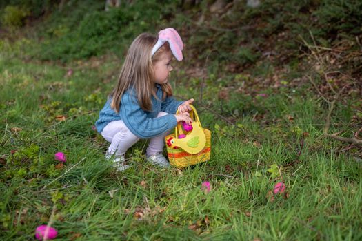 Girl with bunny ears collects the eggs in a basket for Easter