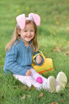 Girl with bunny ears collects chocolate eggs in a basket for Easter