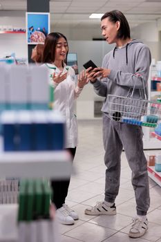 Pharmacist and client talking about pharmaceutics on smartphone, man looking to buy drugs and prescription medicine. Examining boxes of medical supplements and vitamins products.