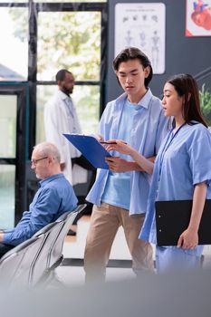 Asian assistant explaining medical report to patient after showing where need to sign before start examination during checkup visit in hospital waiting area. Health care service and concept