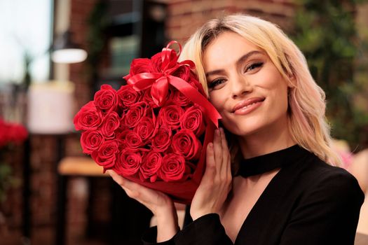 Cute girlfriend posing with valentines day red roses bouquet, receiving romantic gift from boyfriend during love holdiday. Attractive woman smiling at camera, holding flowers in heart shaped box