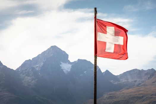 Swiss flag and Bernina mountain range with glaciers in the Alps, Engadine, Switzerland