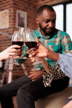 Closeup shot of unrecognizable, different ethnicities group of people hands, toasting, celebrating with wine glasses. Adult african american man clinking glasses at party friends.