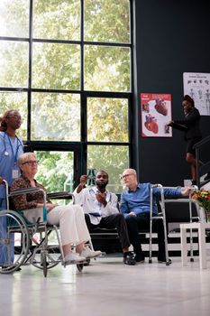 African american doctor holding lungs radiography explaining medical expertise to disabled senior patient during checkup visit appointment in hospital waiting area. Medicine service and concept