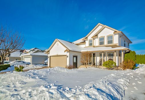 Family house with driveway and front yard in snow on winter sunny day. Luxury residential house with double garage on winter season