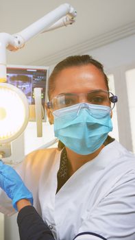 Patient pov visiting dental clinic for surgery treating affected mass. Doctor and nurse working together in modern orthodontic office, lighting the lamp and examining person wearing protection mask.