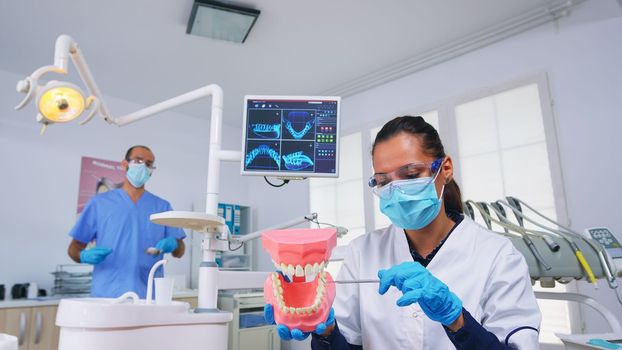 Patient pov of dentist showing correct way of cleaning teeth wearing in dental office using teeth medical skeleton accessory. Stomatolog wearing protection mask during heatlhcare check
