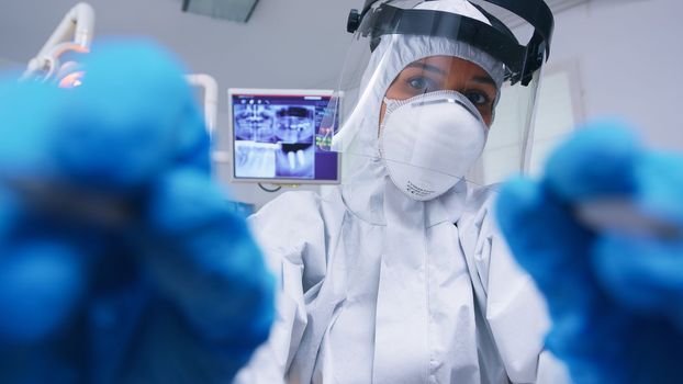 Pov of dentist in ppe suit against covid working on patient mouth hygine in dental office with new normal. Stomatolog wearing safety gear against coronavirus during heatlhcare check of patient.