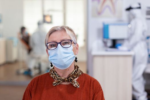Portrait of retired patient in dental office looking on camera wearing face mask sitting on chair in waiting room clinic while doctor working. Concept of new normal dentist visit in coronavirus outbreak.