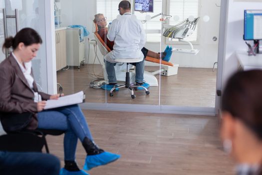 Senior woman sitting on chair in dental office listening dentist talking about diagnosis for teeth cavity looking at digital x-ray radiography. Patients filling form in waiting area.