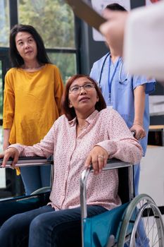 Senior patient in wheelchair having medical appointment talking with elderly doctor before physical examination in hospital waiting area. Physician explaining disease diagnosis discussing treatment