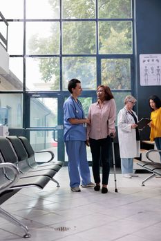 Nurse giving support to injured woman trying to walk with cane, using walking aid to recover after leg fracture injury. Assistant helping senior patient to cure physical condition, physiotherapy.